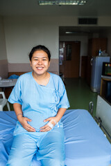 Fototapeta premium Portrait of patient pregnant Asian woman sitting smiling and happy on the bed in the hospital. Breast Cancer, Osteoporosis, Diabetes, Emergency Room