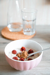 Milk oatmeal with raspberry berries in a glass white bowl on the table in the kitchen.