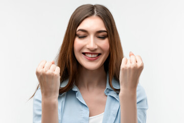 Fototapeta premium Image of young happy woman smiling and making winner gesture. Studio shot, white background, isolated