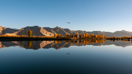 A plane is flying over mountains and rivers at sunrise. 