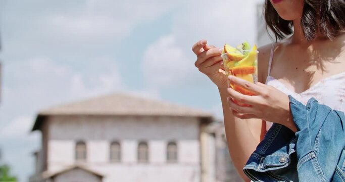 Woman eating fruit salad in city or old town. Tourist have a break eating a fruit salad i n sunny day. Detail of woman picking with fork a fruit salad