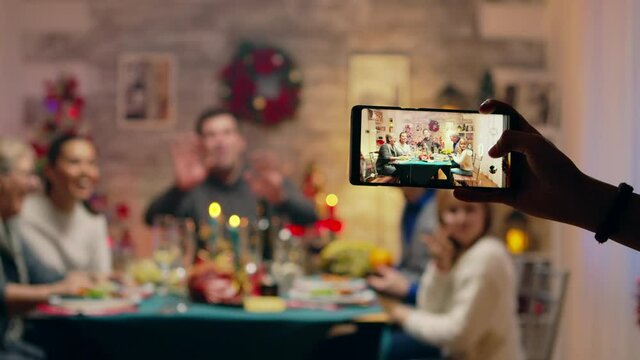 Girl taking photos of her family using smartphone at christmas reunion. Traditional festive christmas dinner in multigenerational family. Enjoying xmas meal feast in decorated room. Big family reunion