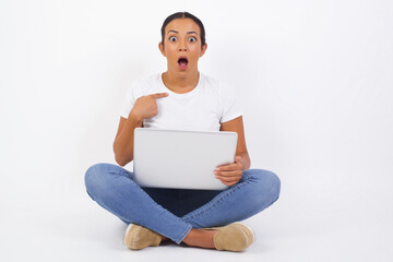 Surprised beautiful female student being in stupor shocked, has astonished expression pointing at herself with finger saying: Who me? Isolated over gray background.