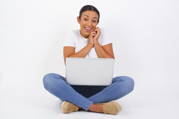 Dreamy charming young female with pleasant expression, keeps hands crossed near face, excited about something pleasant, poses against gray background.