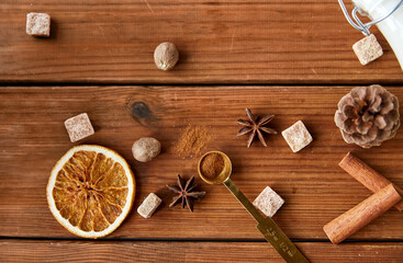 christmas and seasonal drinks concept - aromatic spices, brown sugar, nutmeg and pine cone on wooden background