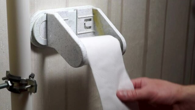 Hand tears pieces of toilet paper from a roll that run out