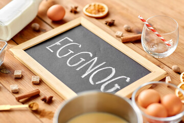 christmas and seasonal drinks concept - eggnog word written on chalkboard, ingredients and aromatic spices on wooden background