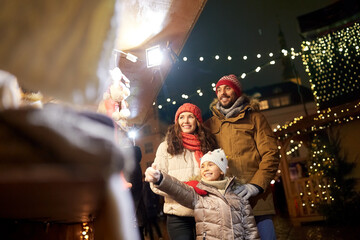 Fototapeta na wymiar family, winter holidays and celebration concept - happy mother, father and little daughter at christmas market on town hall square in tallinn, estonia