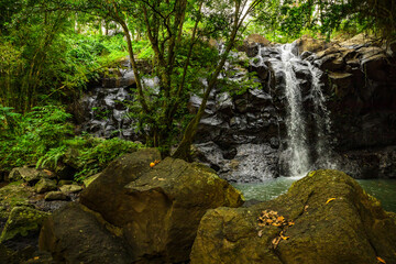 Waterfall landscape. Beautiful hidden waterfall in tropical rainforest. Foreground with big stones. Fast shutter speed. Sing Sing Angin waterfall, Bali, Indonesia