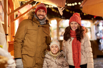 family, winter holidays and celebration concept - happy mother, father and little daughter at christmas market on town hall square in tallinn, estonia
