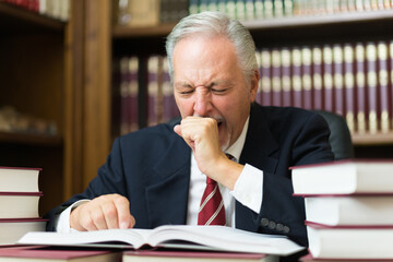 Sleepy business man lawyer yawning. Surrounded by many books
