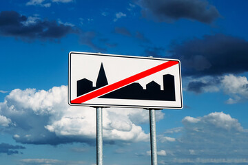 End of built-up area road sign isolated on cloudy sky background. Car travel through countryside.	Leaving city center running away from traffic jams.