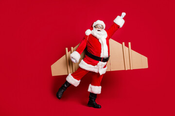 Hero we deserve. Full body size photo of retired childish grandpa white beard jetpack fist up fly save world wear santa x-mas costume coat spectacles headwear isolated red color background
