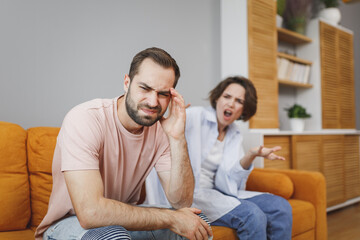 Displeased dissatisfied angry irritated young couple two friends man woman in casual clothes sitting on couch screaming swearing put hand on head looking aside spending time in living room at home.