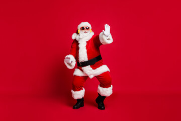 Full body size photo of pensioner old man grey beard chilling middle dance floor wear santa costume gloves coat belt sunglass headwear earphones black boots isolated red color background
