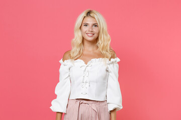 Smiling cheerful charming pretty cute beautiful attractive young blonde woman 20s wearing white casual clothes standing and looking camera isolated on bright pink colour background, studio portrait.