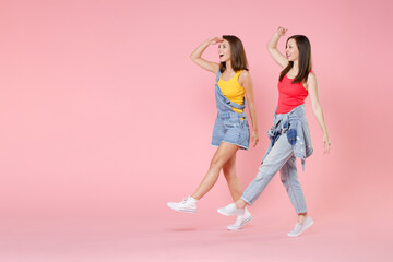 Full length portrait of two excited young brunette women friends in casual denim clothes posing holding hand at forehead looking far away distance isolated on pastel pink colour background studio.