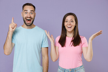 Excited young couple two friends man woman 20s in blue pink empty blank t-shirts holding index...