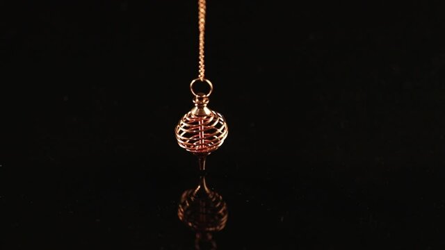 Golden pendulum in the form of a spiral swings against a black background
