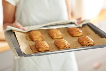 food cooking, culinary and people concept - young woman with towel holding hot baking tray with jam pies at home kitchen