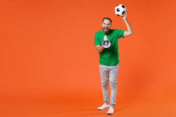 Fototapeta na wymiar Full length portrait funny man football fan in basic green t-shirt cheer up support favorite team with soccer ball screaming in megaphone isolated on orange background. People sport leisure concept.