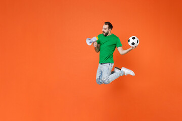 Fototapeta na wymiar Full length portrait excited man football fan in green t-shirt cheer up support favorite team with soccer ball scream in megaphone jumping isolated on orange background. People sport leisure concept.