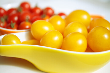 Yellow and red cherry tomatoes. Yellow cherry tomatoes lie in a yellow bowl against a blurry background of red small tomatoes. Autumn collection of vegetables. Bright harvest