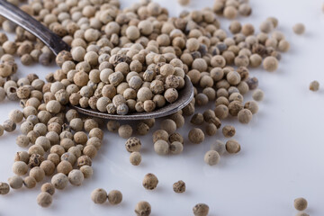 white peppercorns in spoon on white background