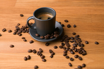A grey cup of coffee on a wooden table with fresh coffee beans around with against a dark background