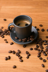 A grey cup of coffee on a wooden table with fresh coffee beans around with against a dark background