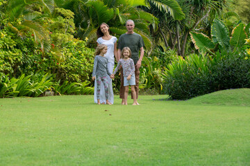 Obraz premium Young happy family walking in tropical park or gaden with palm trees. Summer exotic vacation