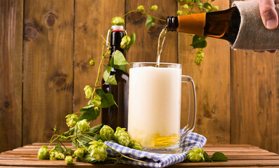 Beer. Cold Craft light Beer in a glass with water drops. Pint of Beer close up on a wooden background. Beer is pouring from the bottle. Border design. 