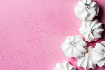 White marshmallows on a pink background. Meringues lie on a bright table