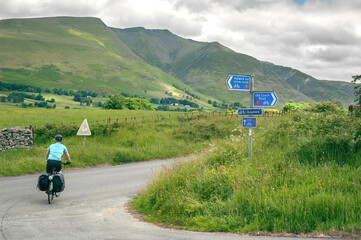 Lone cyclist riding the Coast to Coast (C2C) cycle route through the hills of the Lake District,...