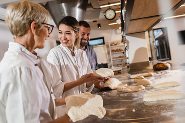 Group of bakers in uniform preparing dough for baking bread in modern manufacturing.	