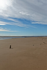 The smooth wide sandy beach at Tentsmuir Point on the Tay Estuary, with a small weathered wooden Marker standing upright in the sand.