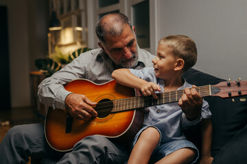 grandfather and his grandson relaxing on sofa at home playing guitar