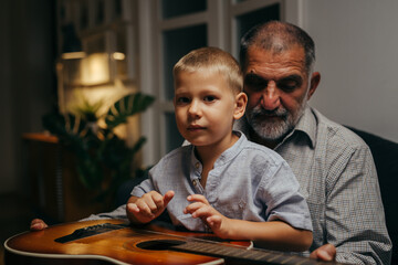 grandfather and his grandson relaxing on sofa at home playing guitar