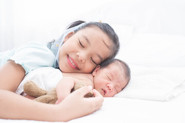 little sister hugging her newborn brother. toddler kid meeting new sibling. love, trust and tenderness. cute girl and new born baby boy relax in a white bedroom. family with children at home.