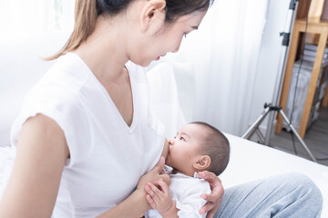Obraz premium Mother breastfeeding her newborn baby beside window. Milk from mom’s breast is a natural medicine for children. Woman feeding baby. A Young mother holding her baby child.