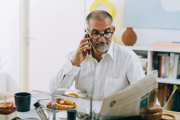 middle aged man reading newspaper at home during breakfast