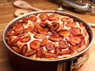 Delicious plum cake made from organic ingredients in a baking pan on a rustic kitchen table, seasonal food or healthy eating