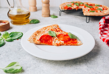Pepperoni pizza slice on plate on light gray background. Traditional Italian fastfood. With red white checkered towel.
