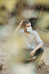 Selective focus shot of an attractive male sitting on the ground and wearing a facial mask