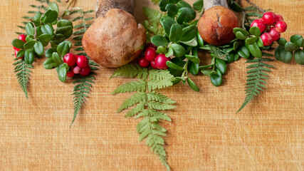 Border of wild mushrooms, lingonberry branches with red ripe berries and fern leaves on wooden textured background