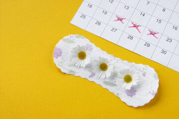 Menstrual pads with chamomiles on menstruation period calendar on yellow background.