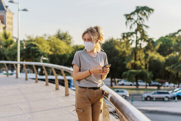 Young Caucasian female wearing a mask against coronavirus looking at the city at the sunset