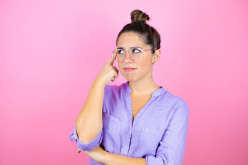 Young beautiful woman wearing glasses over isolated pink background confuse and wonder about question. Uncertain with doubt, thinking with hand on head