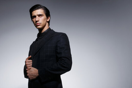 Profile portrait of handsome young man in black stylish suit, isolated on grey background. Horizontal view.