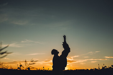 Silhouette of happy man holding his woman on his hands, while the she raising her arms at sunset.  Happy couple at sunset. Copy space.